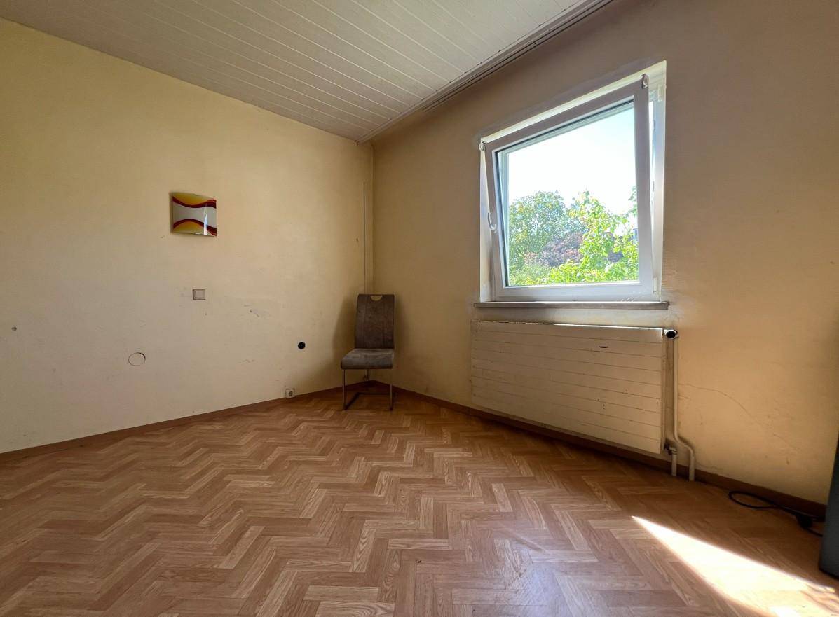 Helles Zimmer mit Laminatboden, großem Fenster und Heizkörper, bietet viel Tageslicht.