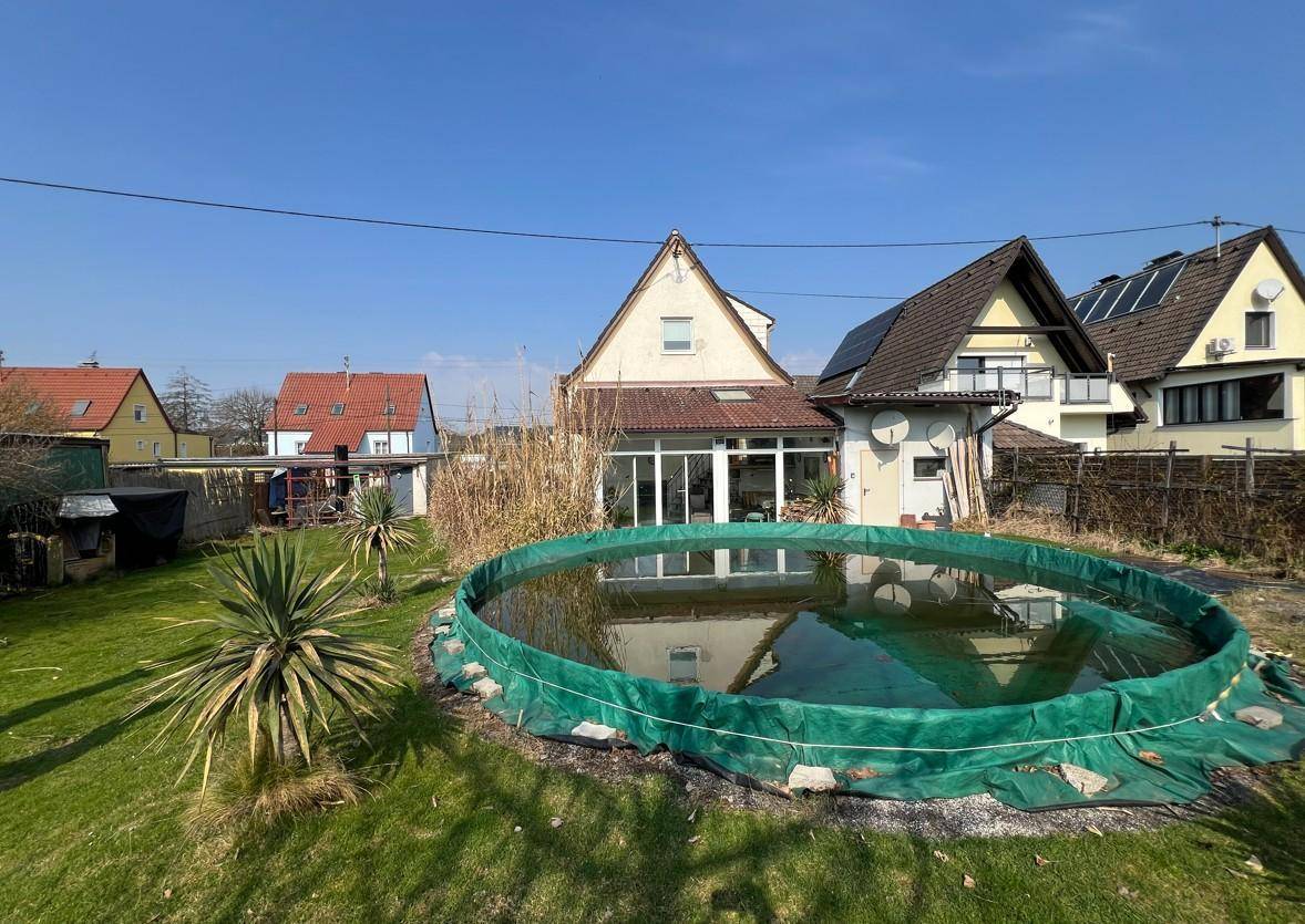 Hinterer Gartenbereich mit Aufstellpool, Wintergarten und benachbarten Häusern.