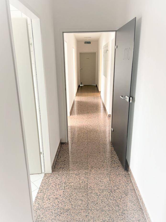 Langer, heller Flur mit Terrazzoboden und Türen zu den Büroräumen in einem Geschäftsgebäude.