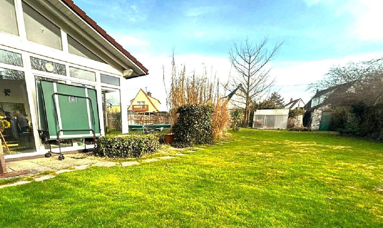 Sonniger Gartenbereich mit Rasenfläche, Tischtennisplatte und Blick auf das Haus.