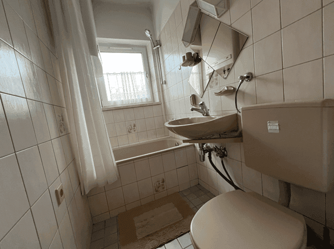 Badezimmer mit Badewanne, WC, Waschbecken und Fenster.