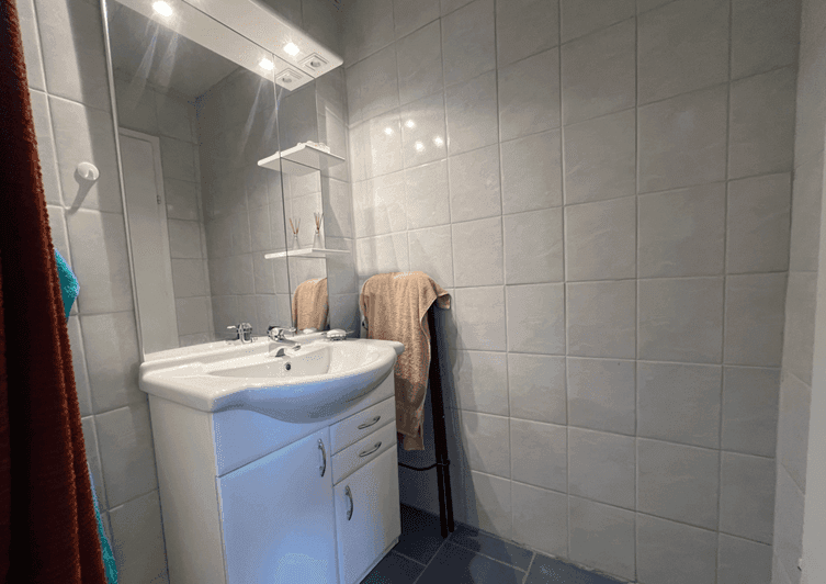 Modernes Badezimmer mit Waschbecken, Spiegelschrank und hellen Wandfliesen.