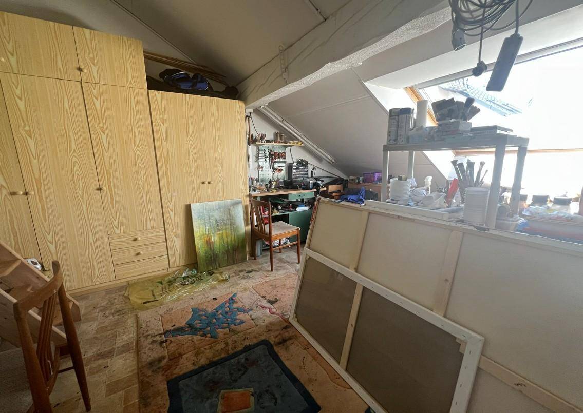 Dachgeschossraum mit Schrägen, Dachfenster und Holzschränken, genutzt als Werkstatt oder Abstellraum.
