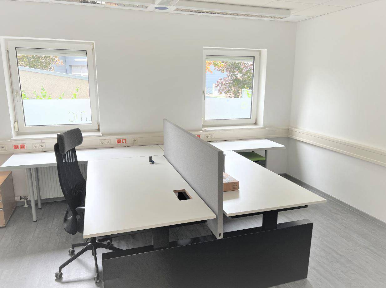 Geräumiger Bürobereich mit mehreren Arbeitsplätzen, Trennwänden und hellen Fenstern.