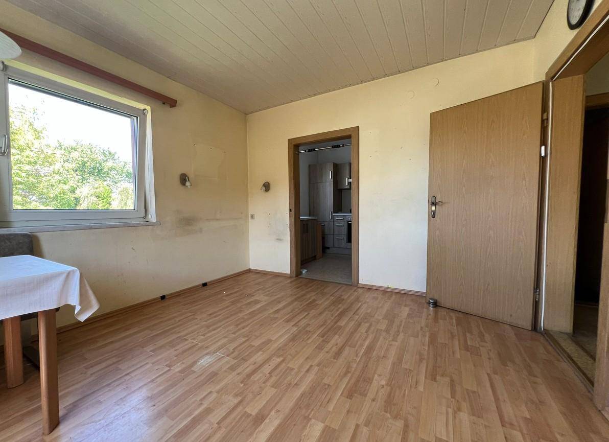 Geräumiger Wohnbereich mit Laminatboden und Fenster, bietet Zugang zu einem weiteren Raum.