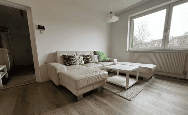 Helles Wohnzimmer mit großem Fenster, beigem Sofa und Heizkörper.