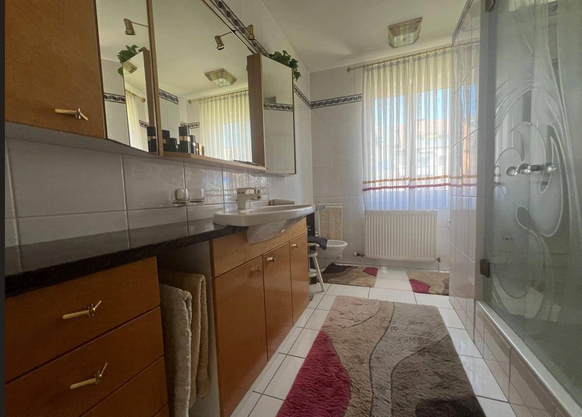 Helles Badezimmer mit Dusche, Einzelwaschbecken, Spiegelschränken und Fenster für Tageslicht.