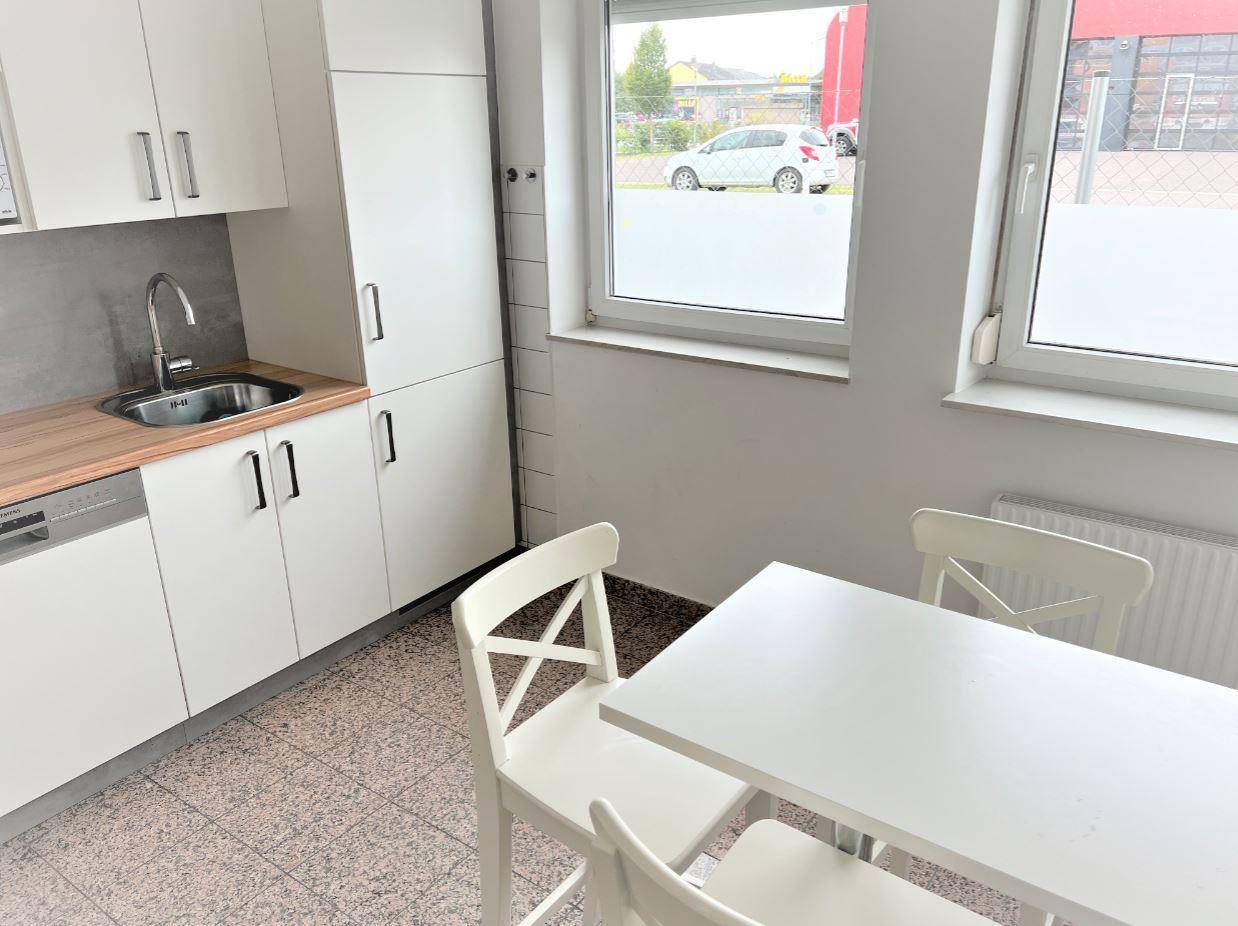 Kleine, funktionale Küche mit weißen Schränken, Holzarbeitsplatte und Essbereich am Fenster.