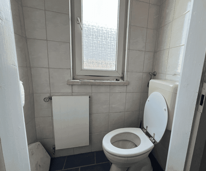 Separate Toilette mit Fenster, Heizkörper und hellen Wandfliesen.