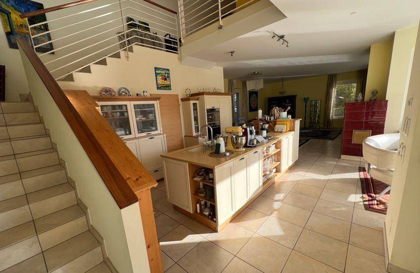 Offene Küche mit Kochinsel und integrierten Geräten, verbunden mit einem Treppenhaus und Wohnbereich.