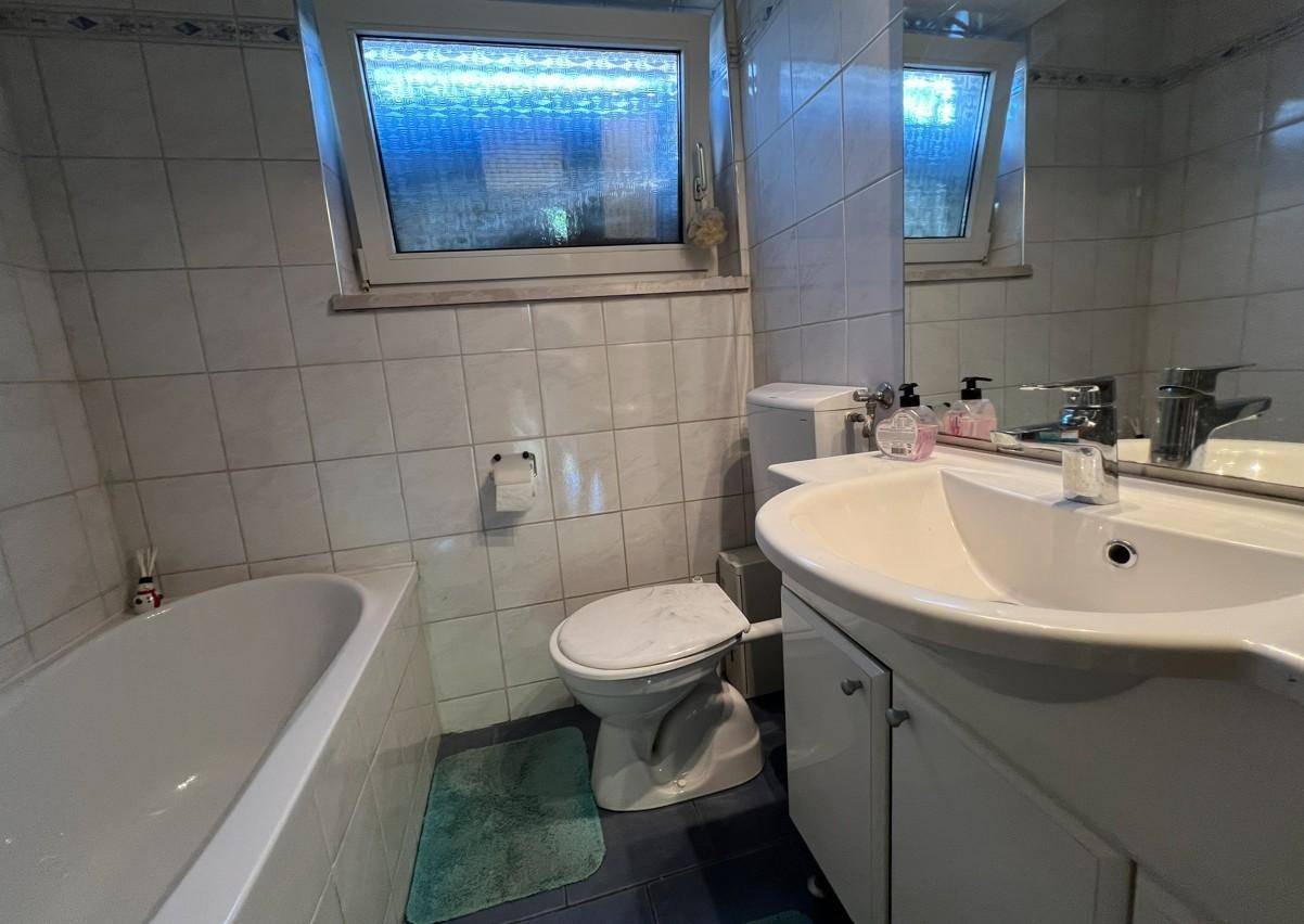 Helles Badezimmer mit Badewanne, WC, Waschbecken und Spiegelschrank, ausgestattet mit weißen Fliesen.