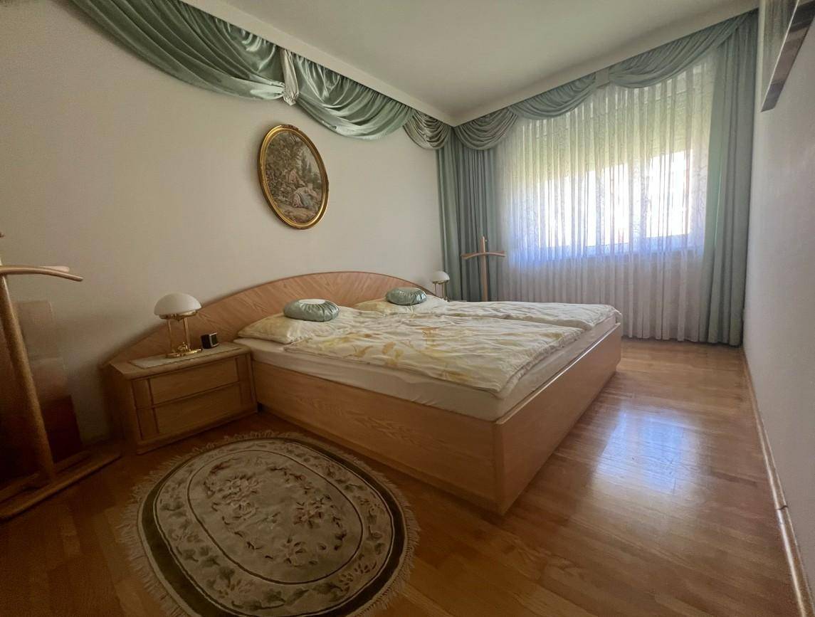 Gemütliches Schlafzimmer mit Doppelbett, Nachttischen und großem Fenster mit eleganten Vorhängen.