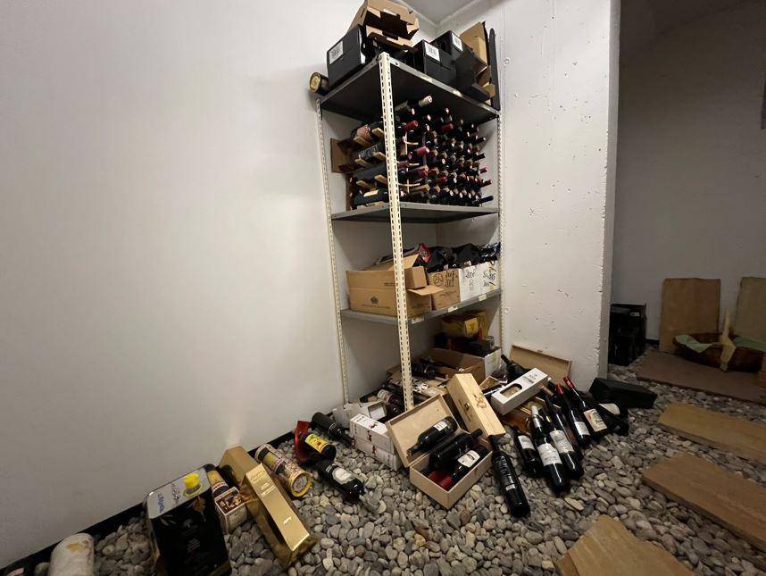 Rustikaler Weinkeller mit Regalen voller Flaschen und einem Kiesboden.