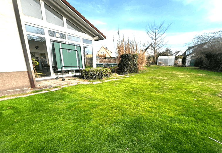 Großer grüner Garten mit Rasenfläche und einer Tischtennisplatte neben dem Haus.