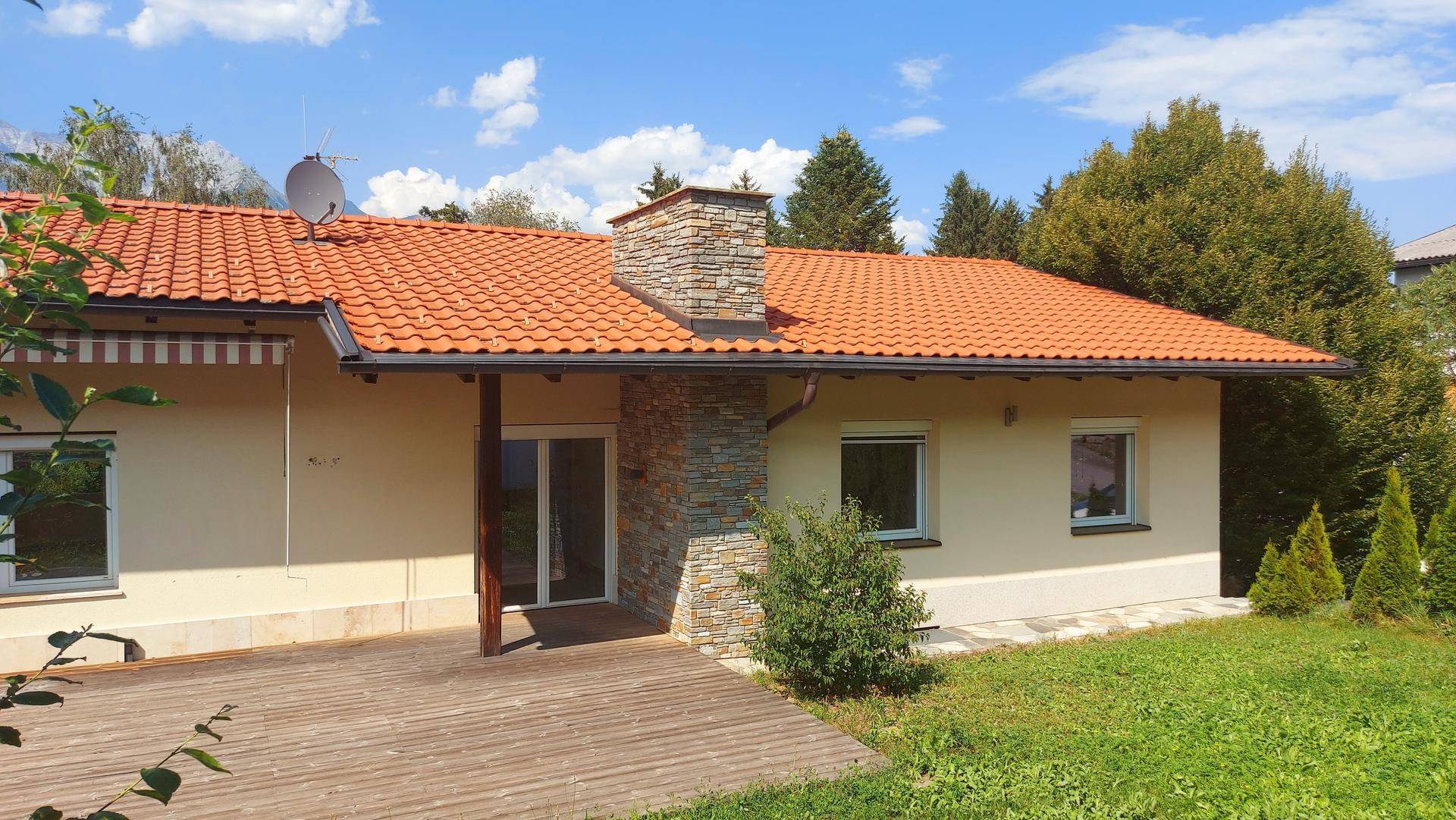 Rückseite des Hauses mit Holzterrasse, Gartenbereich und Panoramablick auf die Berge.