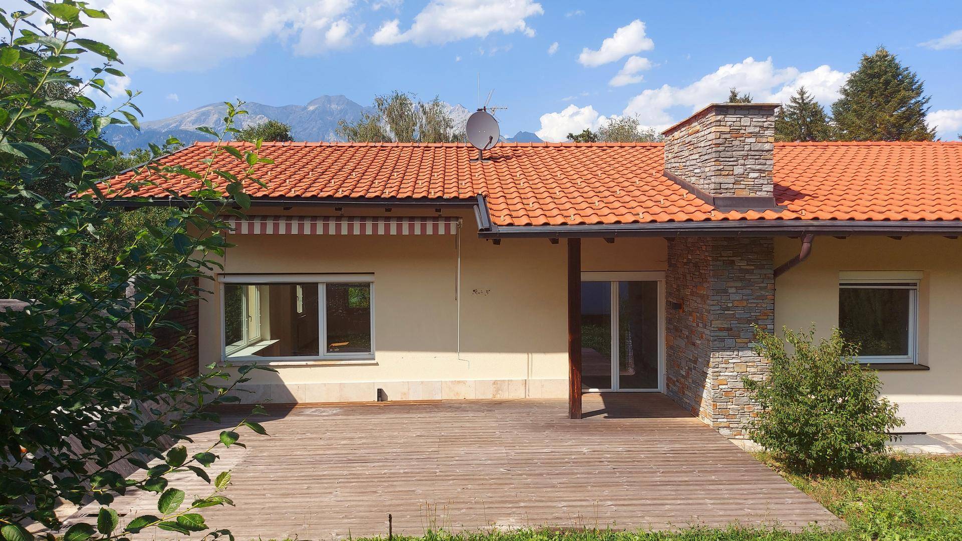 Hausfassade mit großer Holzterrasse, Ziegeldach und Blick auf die umliegende Berglandschaft.