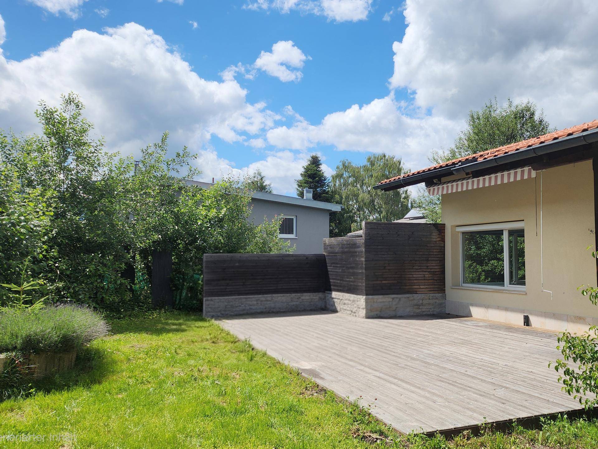 Holzterrasse mit Sichtschutz und angrenzendem Gartenbereich unter bewölktem Himmel.