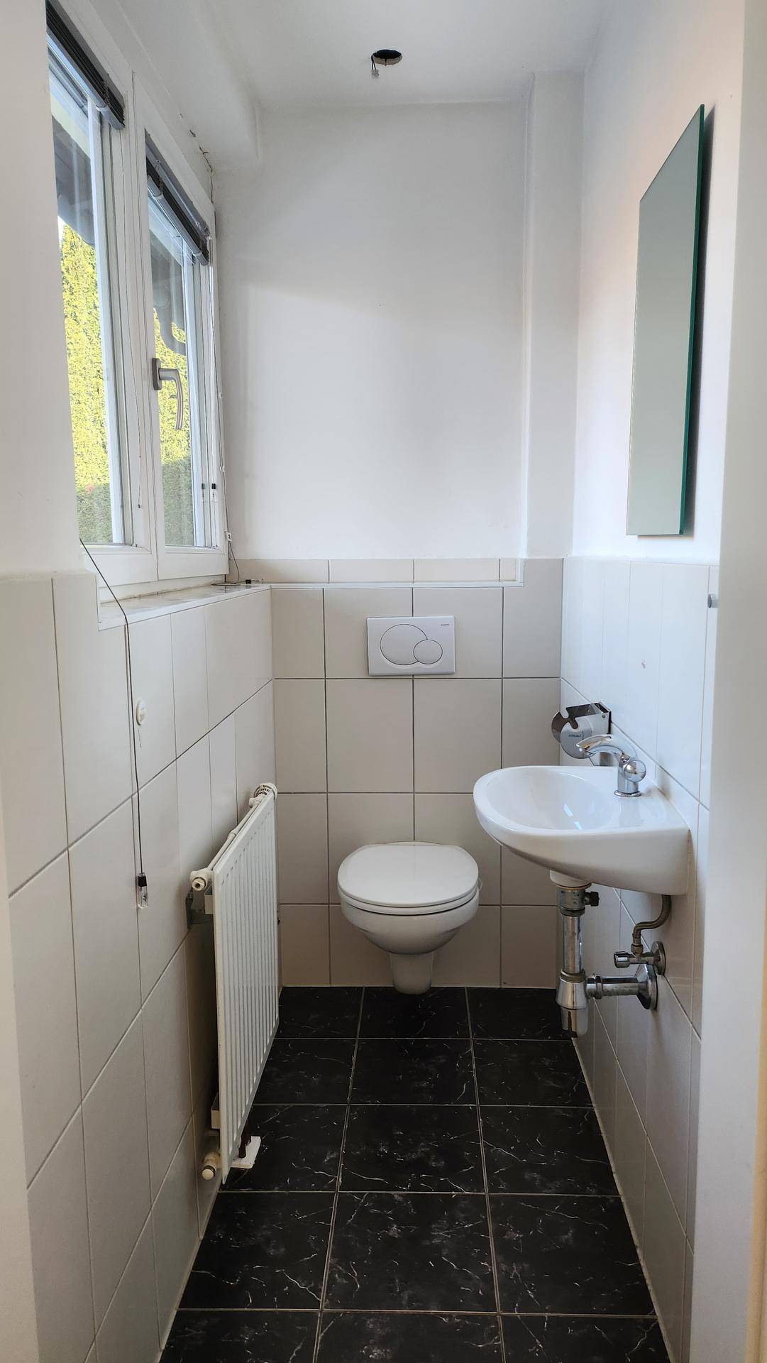 Kleines Gäste-WC mit Fenster, wandhängendem WC und Waschbecken, in hellen Fliesen gehalten.