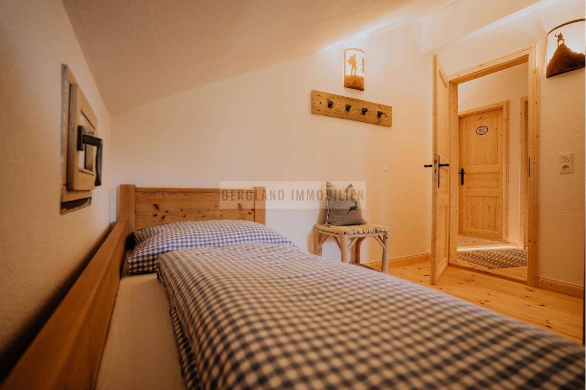 Gemütliches Schlafzimmer mit Einzelbett und Holzrahmen, unter einer Dachschräge gelegen.