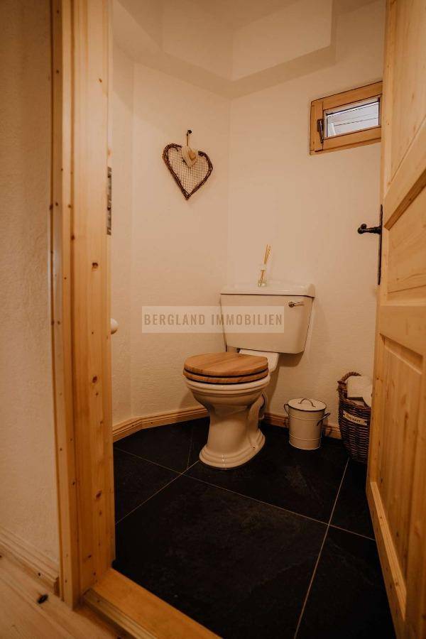Kleines WC mit Fenster und dunklen Fliesen, ausgestattet mit einem Holzsitz.