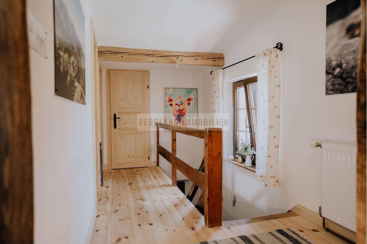 Rustikaler Flur mit Holzgeländer und sichtbaren Deckenbalken, führt zu weiteren Räumen.