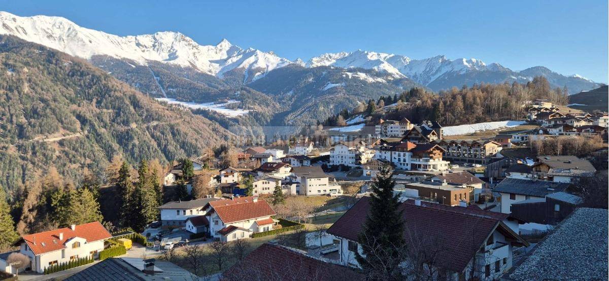 Panoramablick auf ein malerisches Dorf in einem Tal, umgeben von schneebedeckten Bergen.