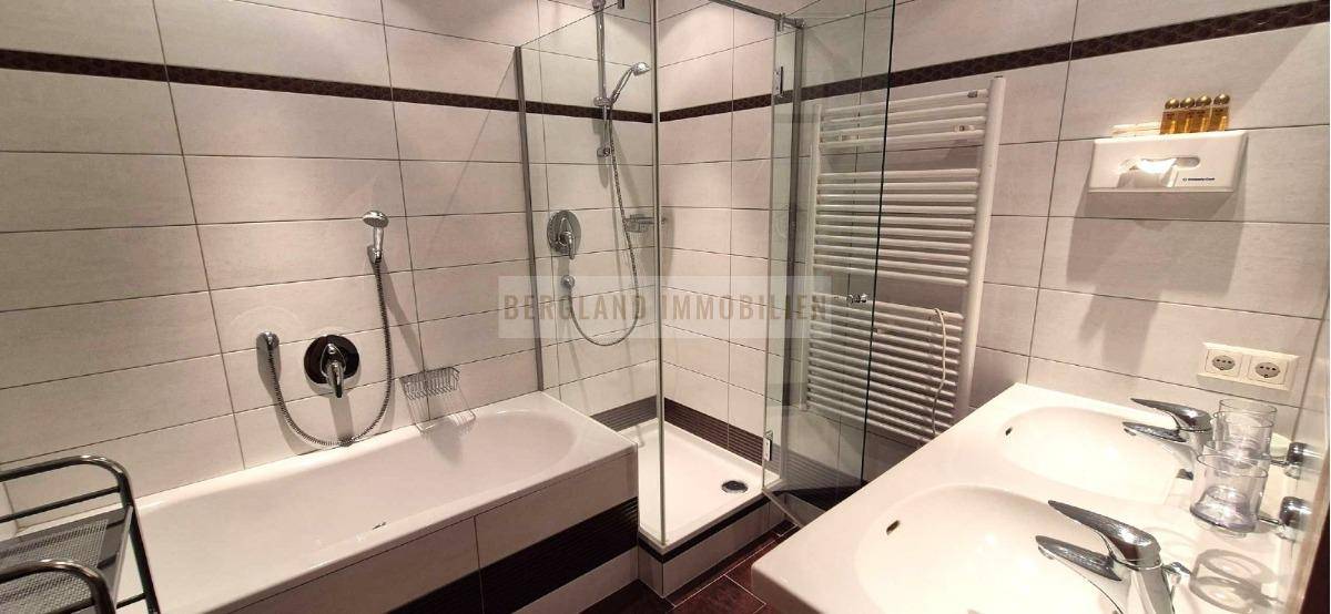 Modernes Badezimmer mit Badewanne, begehbarer Dusche und zwei Waschbecken auf gefliestem Boden.