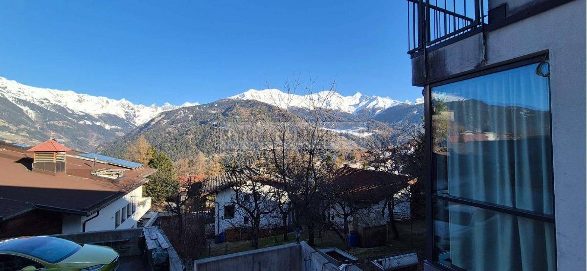 Weitblick auf die majestätischen Alpen und umliegende Häuser von einem Balkon aus.