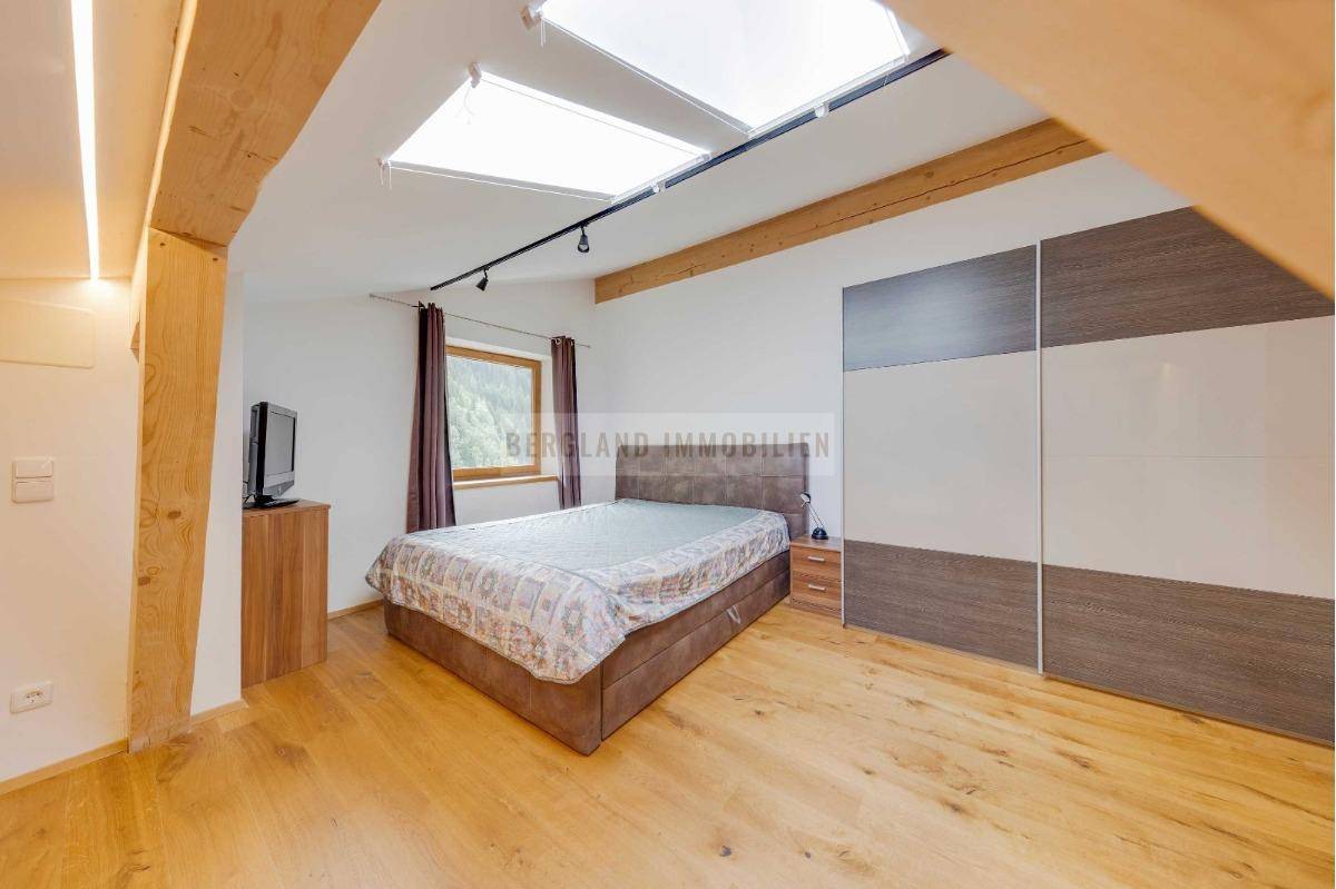 Helles Schlafzimmer im Dachgeschoss mit Holzboden, großem Kleiderschrank und Blick ins Grüne.