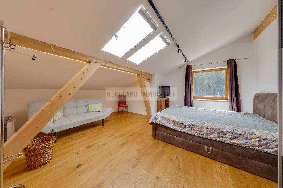 Gemütliches Schlafzimmer im Dachgeschoss mit Holzboden, sichtbaren Balken und Dachfenstern für viel Licht.