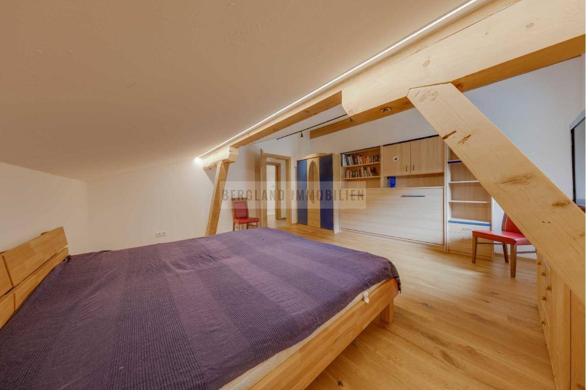 Helles Schlafzimmer im Dachgeschoss mit Holzboden, sichtbaren Holzbalken und integriertem Wandbett.