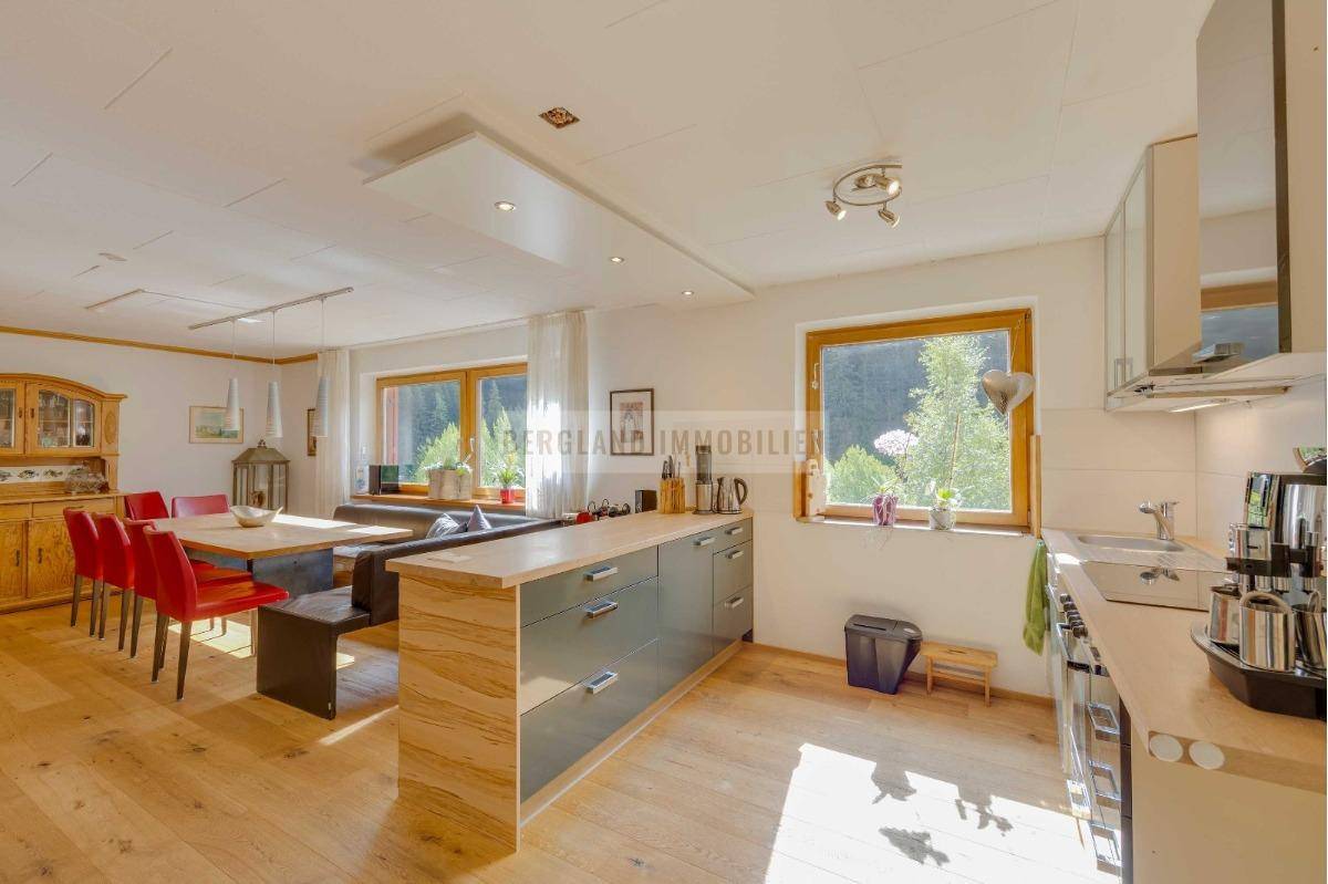 Moderne offene Küche mit Kücheninsel, Essbereich und großen Fenstern mit Blick ins Grüne.