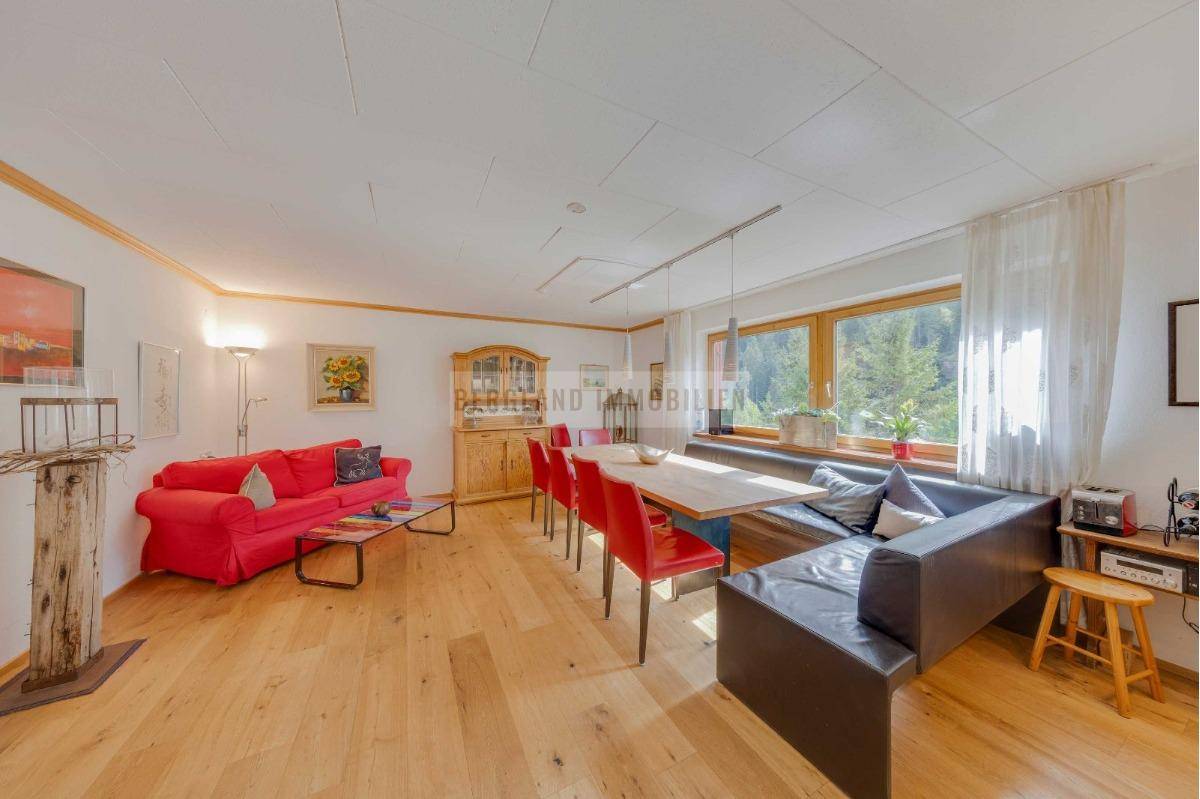 Geräumiger Wohn- und Essbereich mit Holzboden, rotem Sofa und großem Esstisch mit Sitzbank.