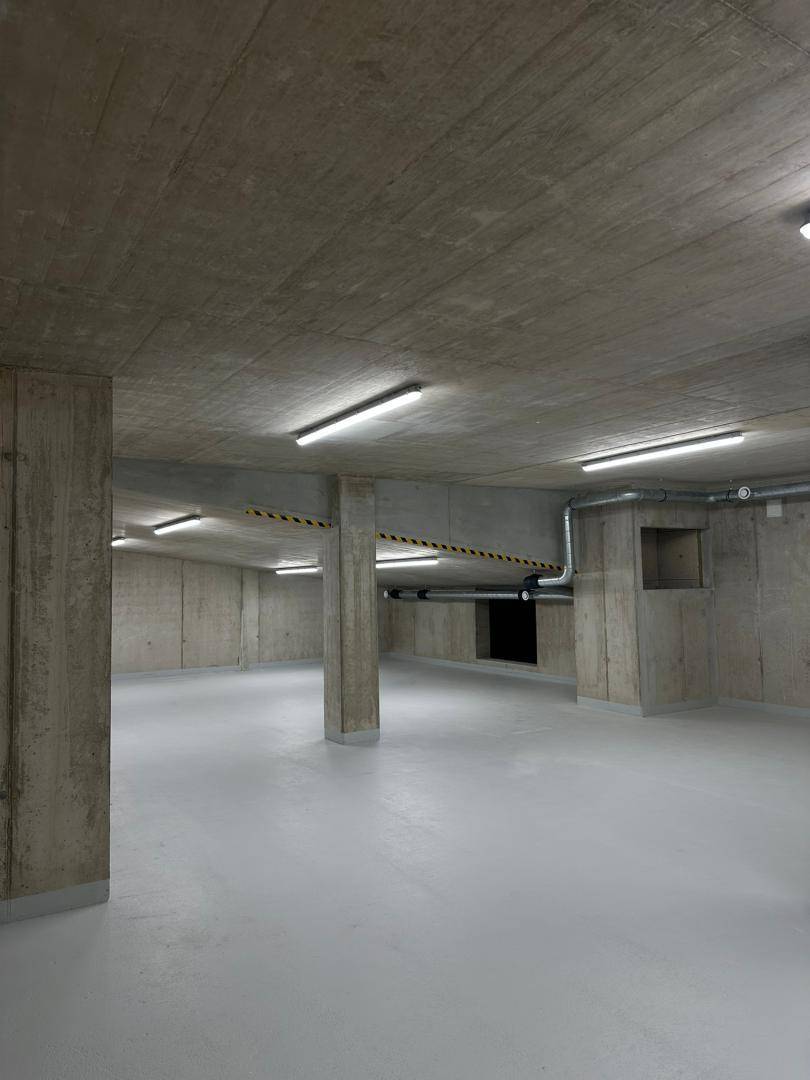 Leere Tiefgarage mit sichtbaren Betonwänden und -decken, beleuchtet von Reihenleuchten und einem hellen Boden.