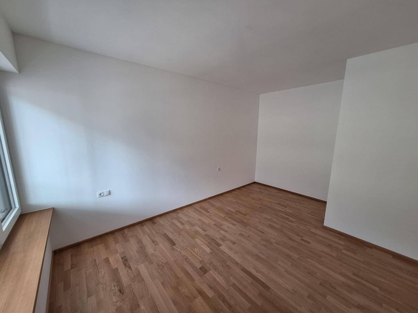 Leeres Schlafzimmer mit hellem Holzboden, weißen Wänden und viel Tageslicht.