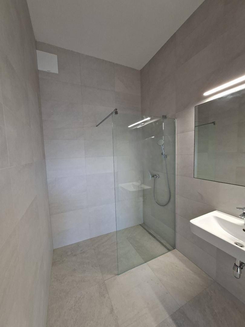 Modernes Badezimmer mit grauen Fliesen, ebenerdiger Dusche und Einzelwaschbecken.