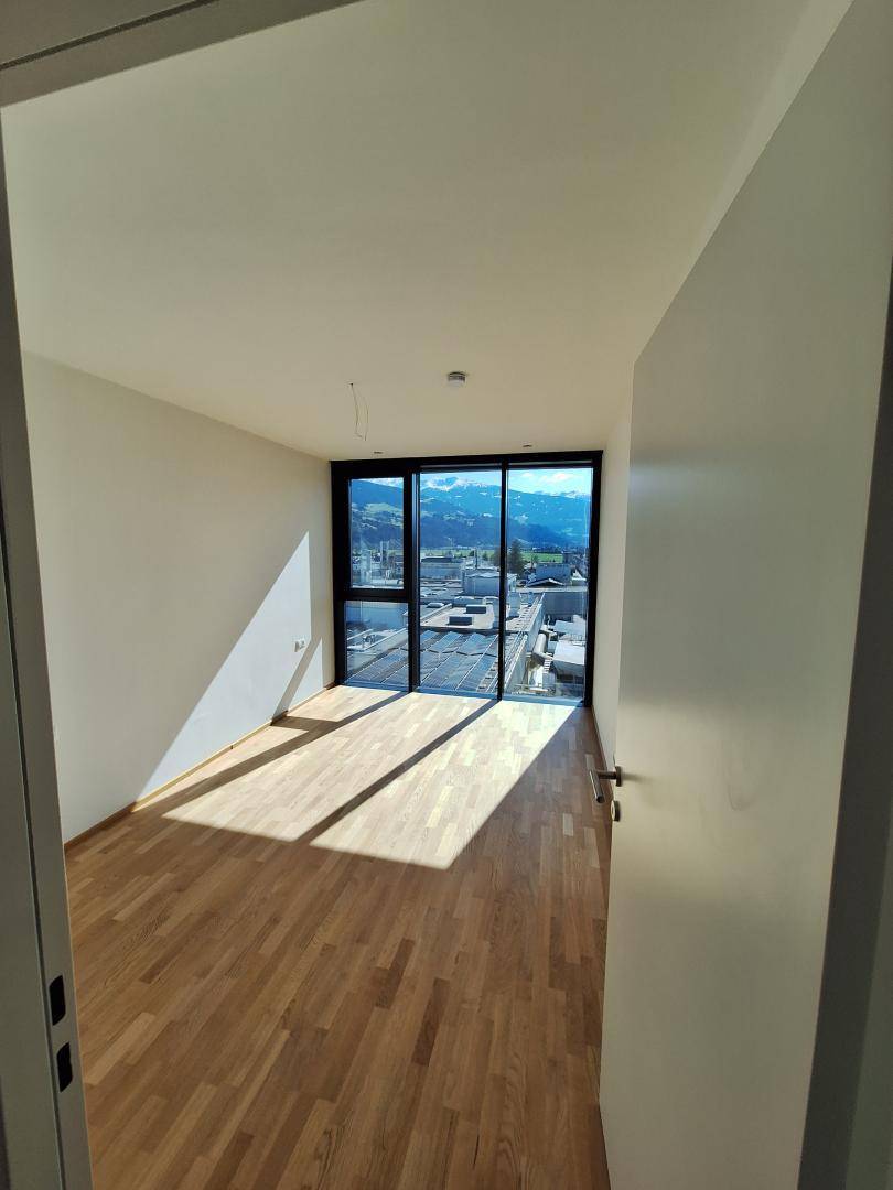 Leeres Schlafzimmer mit großen Fenstern, viel Sonnenlicht und Bergblick.