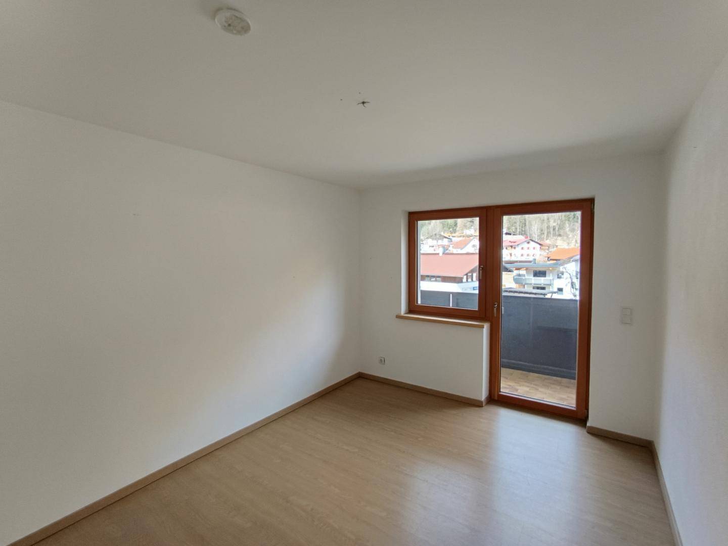 Leerer Raum mit hellem Laminatboden und Zugang zu einem Balkon, ideal für individuelle Gestaltung.