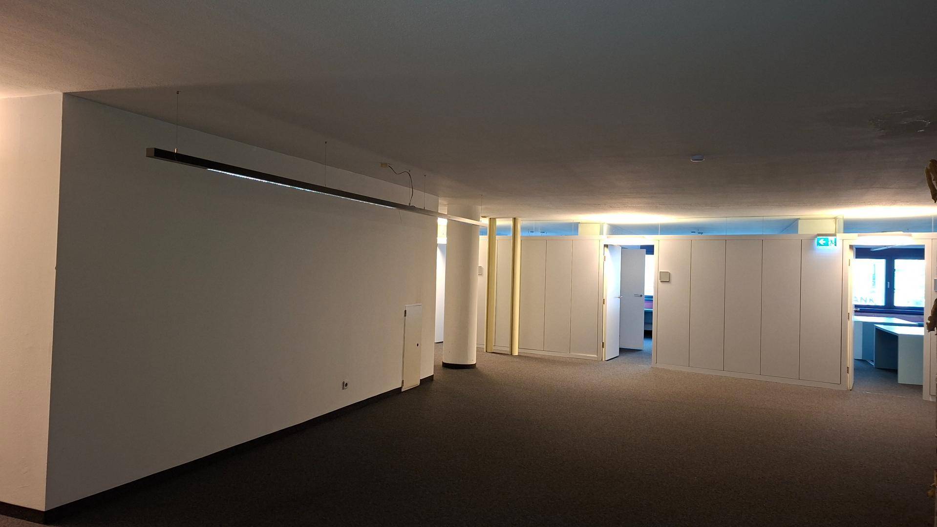 Langer, leerer Bürobereich mit Teppichboden und weißen Wänden, bereit zur Gestaltung.