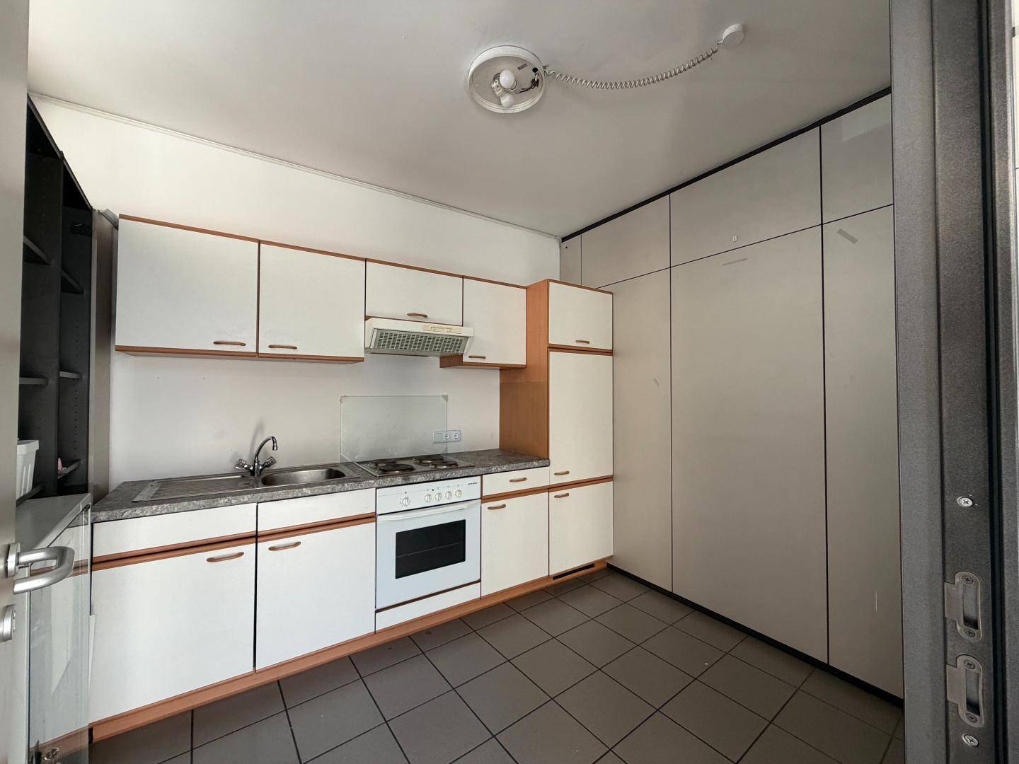 Kleine Küche mit weißen Schränken, Gasherd, Backofen und Dunstabzugshaube, ausgestattet mit Fliesenboden.