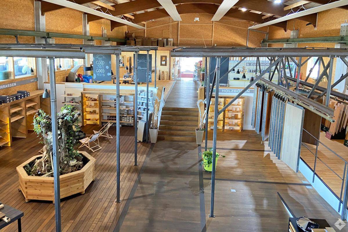 Geräumiger Ausstellungsraum für Holzprodukte mit hohen Decken und sichtbaren Holzbalken.