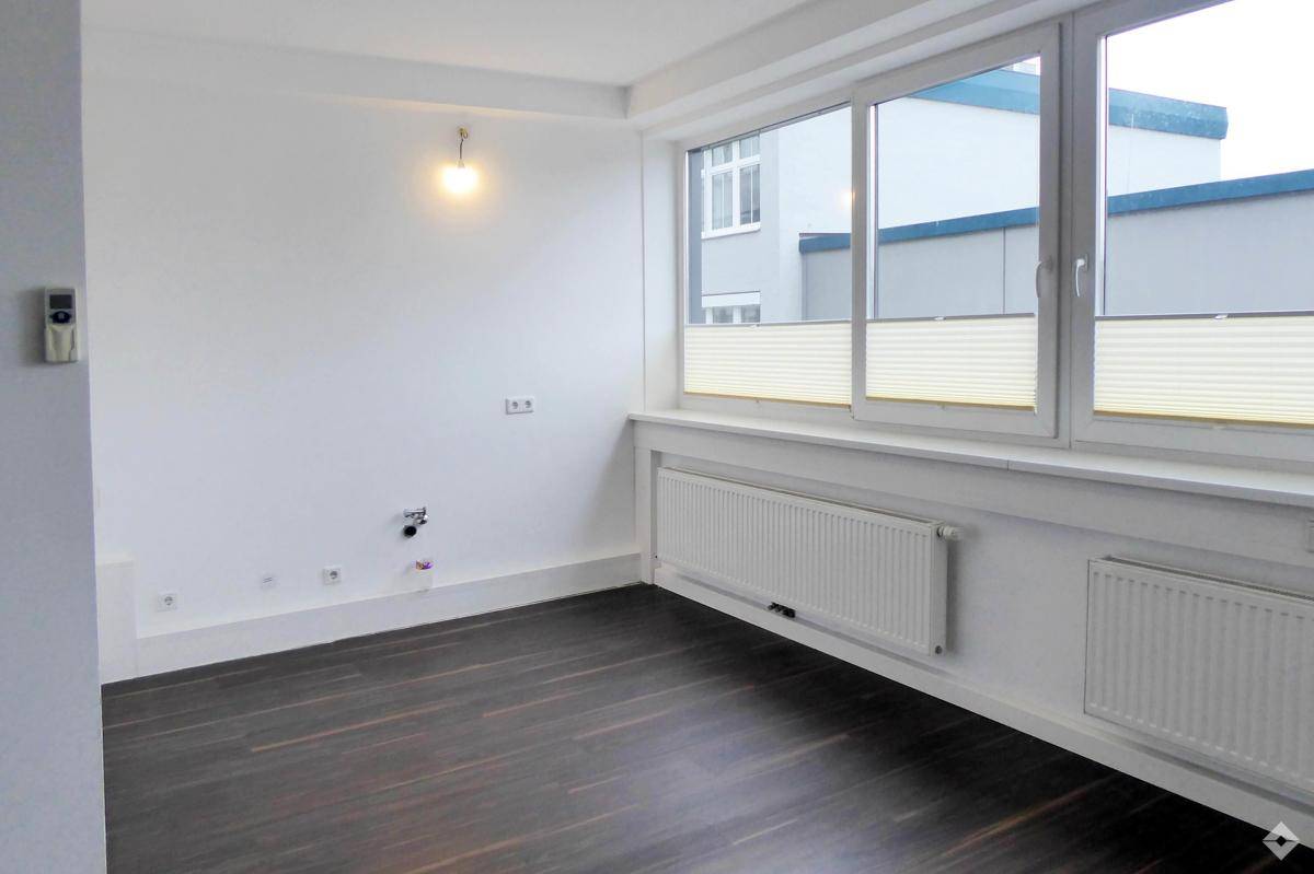 Kleinerer Büroraum mit dunklem Holzboden, großen Fenstern und Anschlüssen an der Wand.