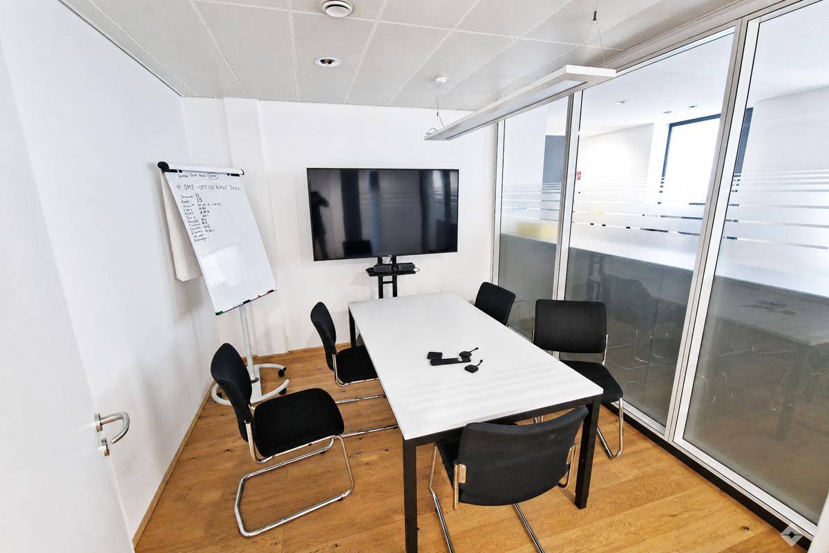 Kleiner Besprechungsraum mit modernem Tisch, Stühlen, Wandfernseher und Whiteboard.