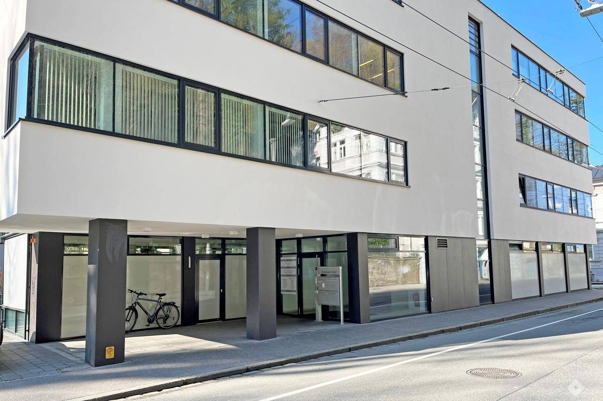 Eingangsbereich eines modernen Bürogebäudes mit Säulen und großen Fenstern im Erdgeschoss, inklusive Fahrradstellplatz.