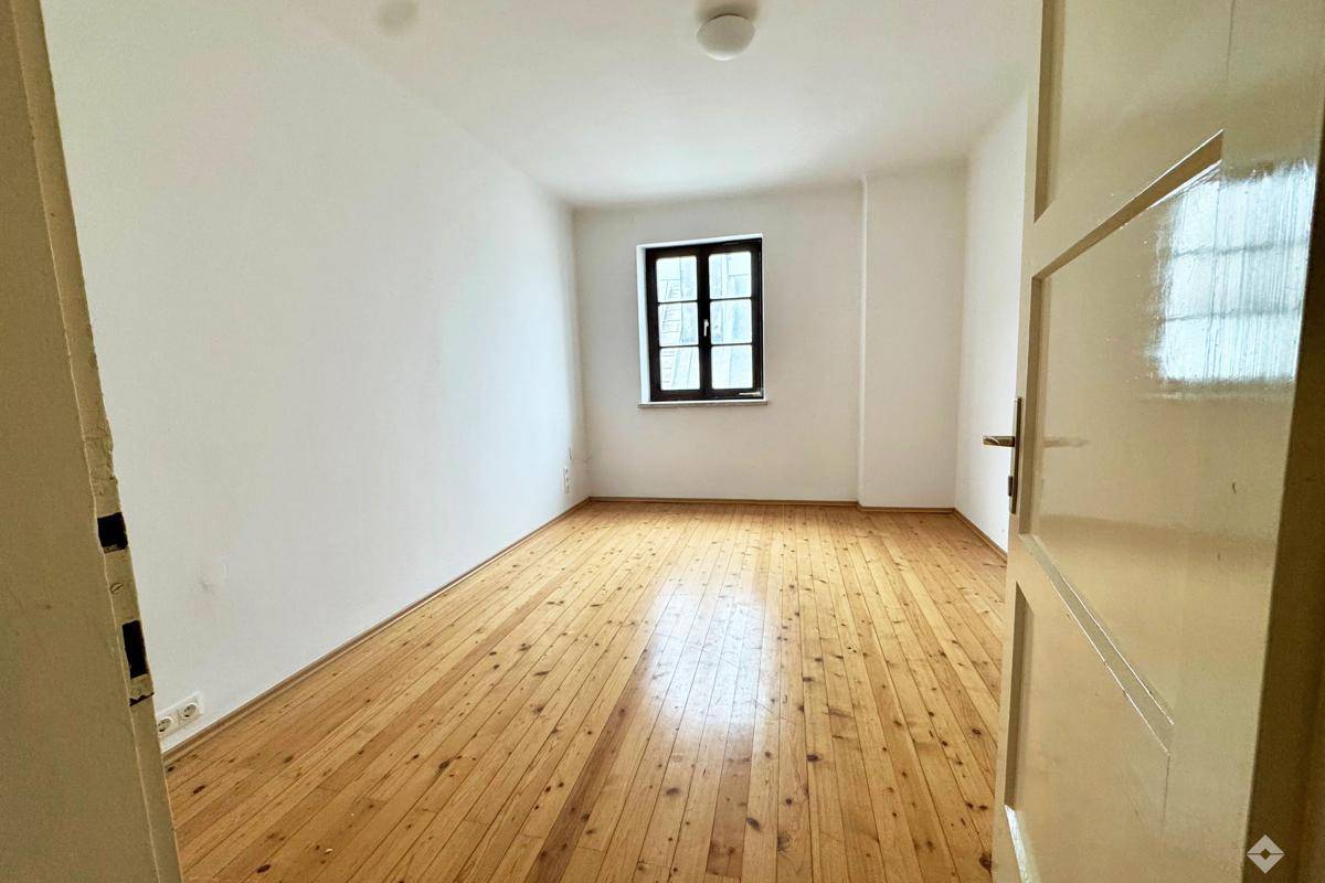 Helles Schlafzimmer mit Holzdielenboden und einem Fenster, das viel Tageslicht hereinlässt.