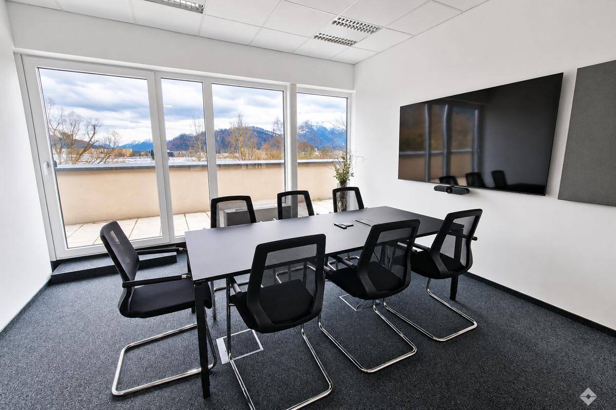 Geräumiger Konferenzraum mit großem Tisch, modernen Stühlen und beeindruckendem Bergblick von der Terrasse.