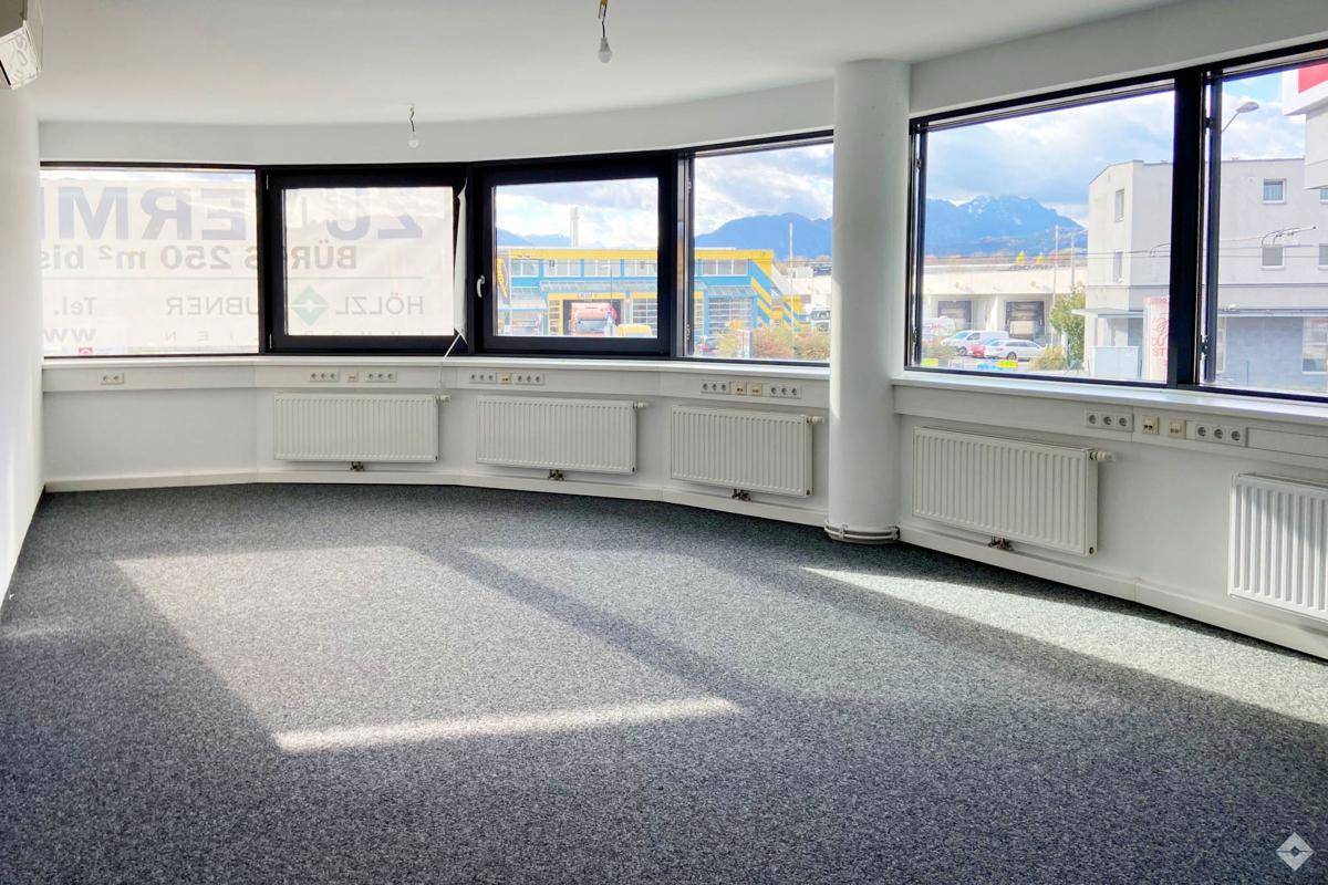 Helles Büro mit Teppichboden, weißen Wänden und Blick auf die umliegende Landschaft.