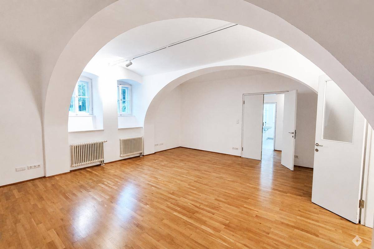Heller Wohnraum mit Holzboden, weißen Wänden und eleganten Gewölbedecken, der zu einem weiteren Zimmer führt.