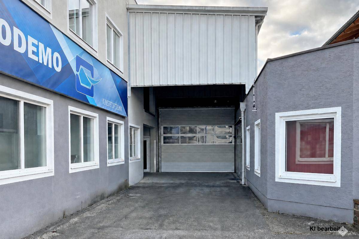 Garageneinfahrt zwischen zwei Gebäudeteilen, einer davon mit blauer Beschriftung und Fenstern.