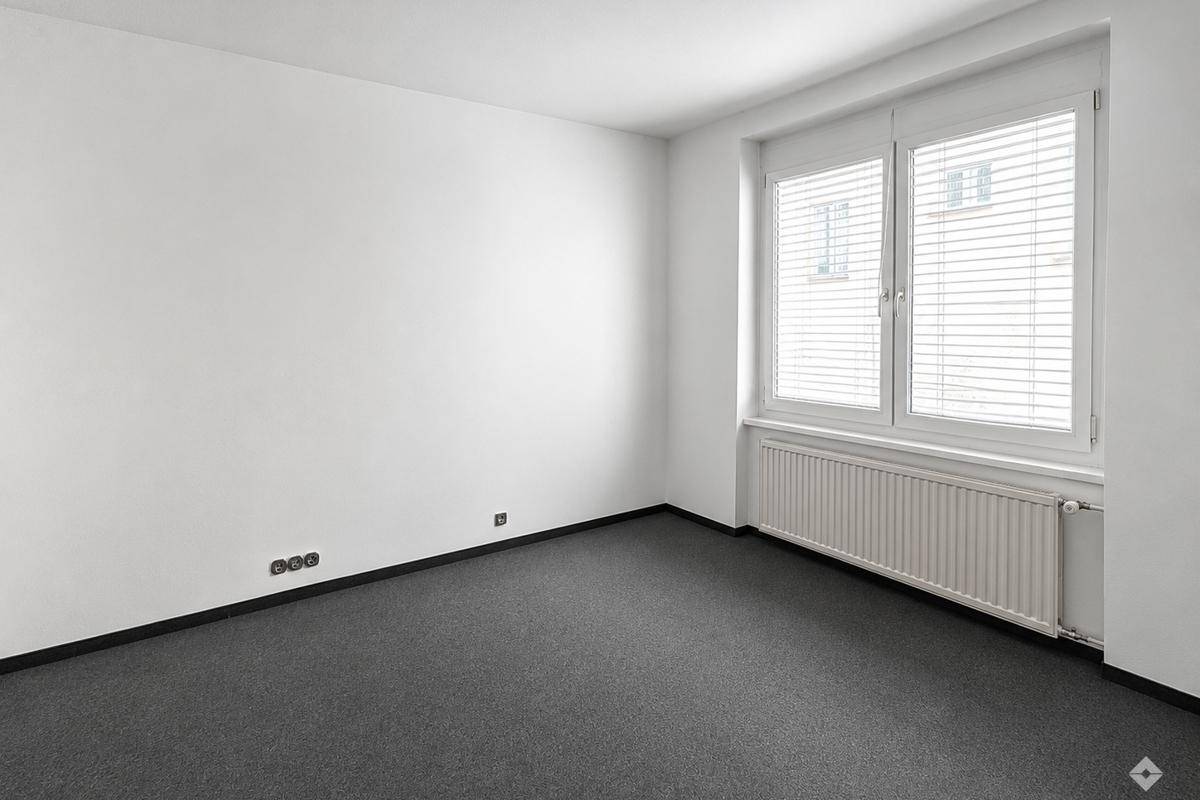 Leeres Büro mit weiß gestrichenen Wänden, Teppichboden und einem Fenster mit Heizkörper.